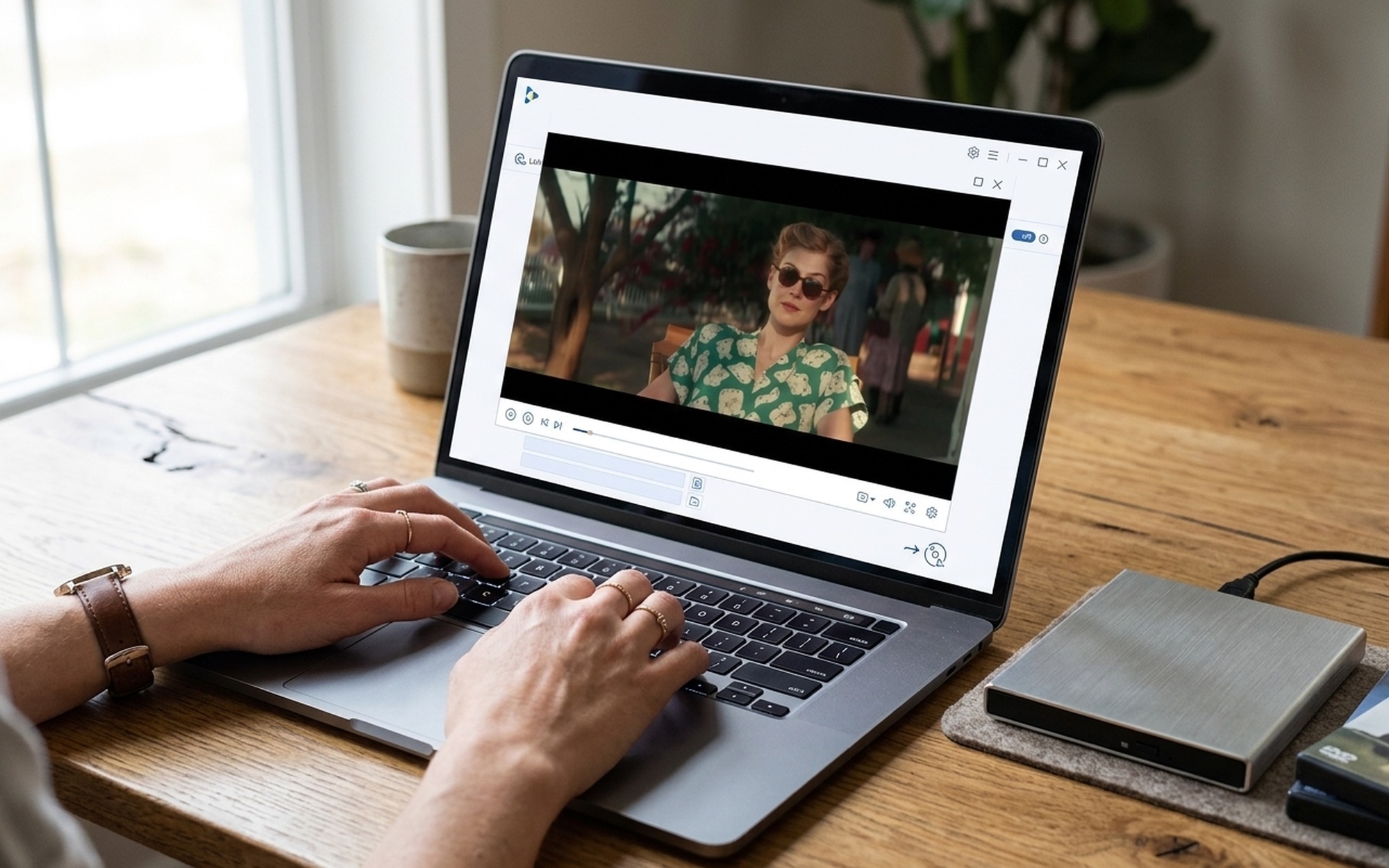 Close-up of hands holding a DVD disc near an open laptop showing a media converter interface on screen