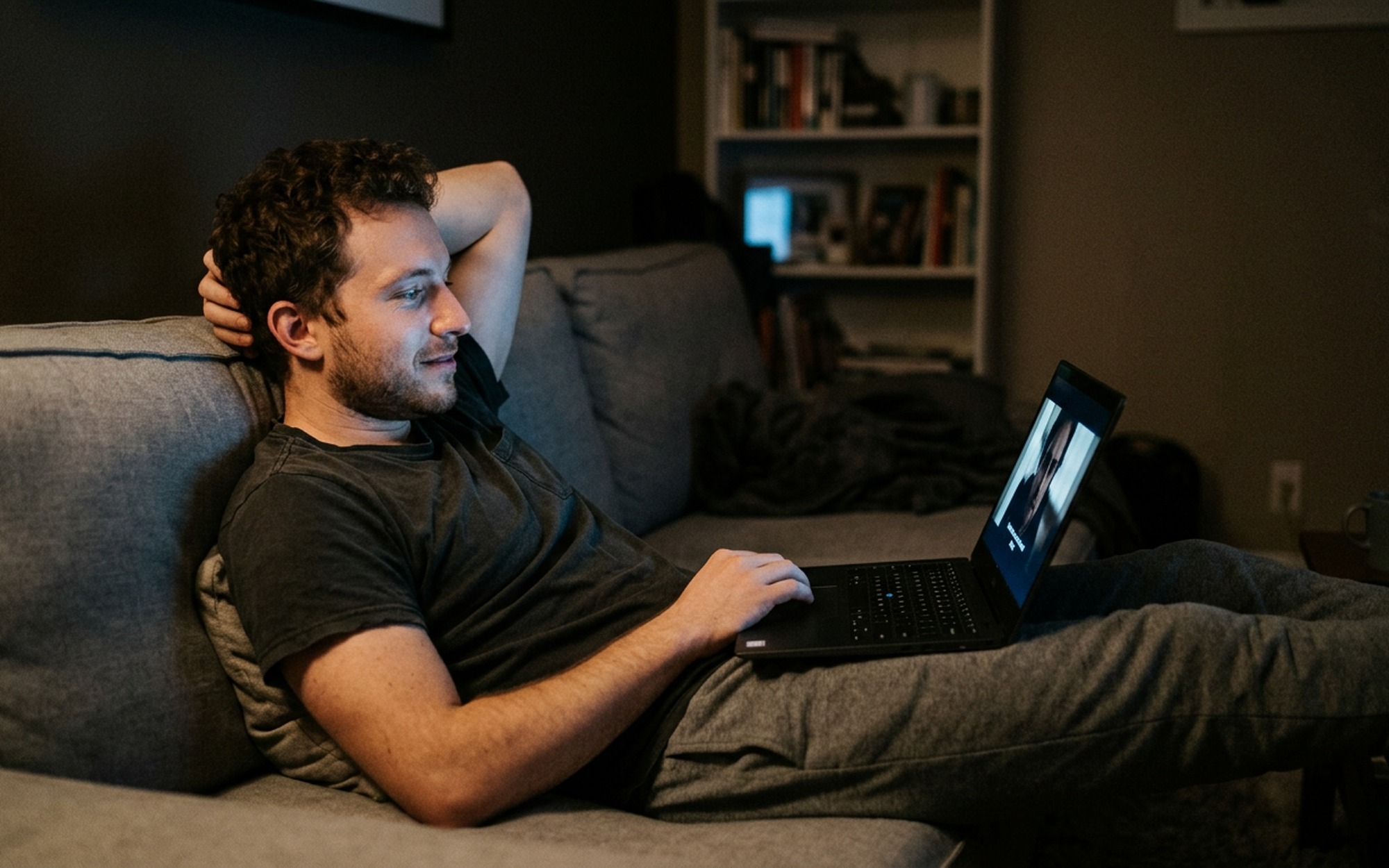 Man watching a free legal movie on a laptop in a darkened living room during an evening movie session
