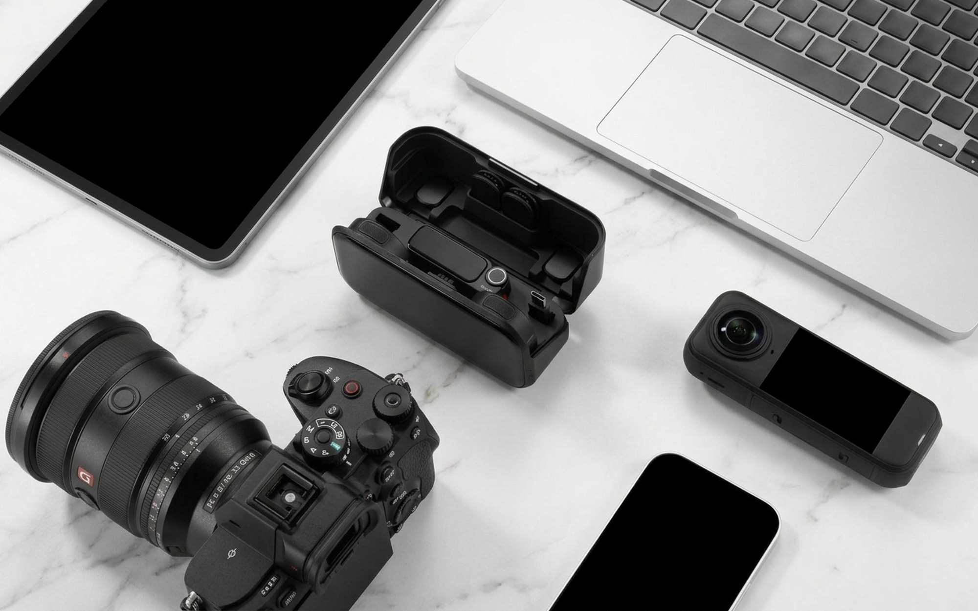 Insta360 Mic Pro wireless microphone kit with charging case open beside a mirrorless camera and laptop on a modern creator desk