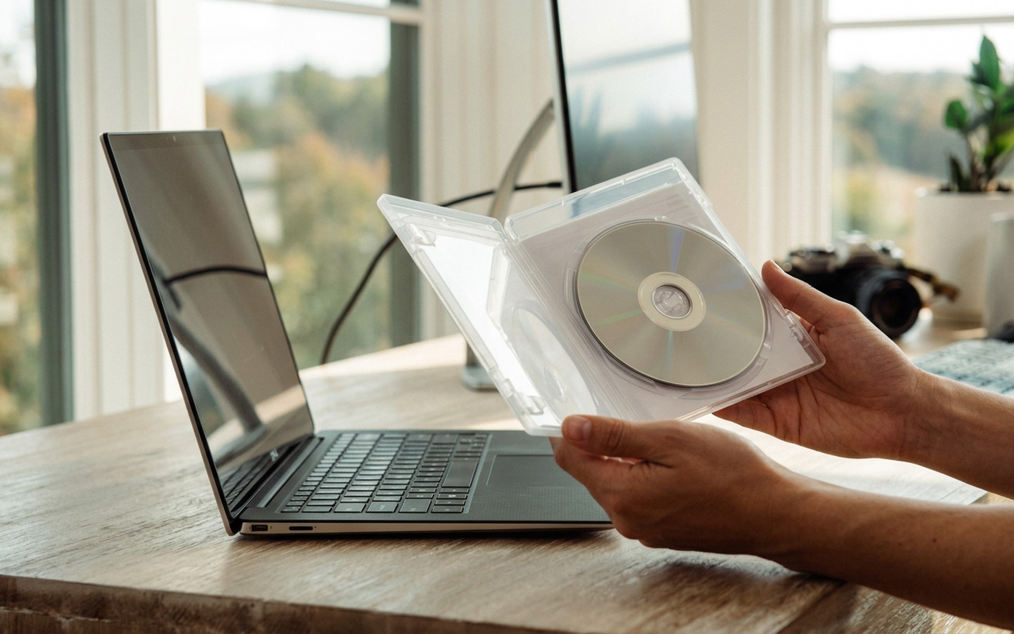 Close-up of a hand holding a Blu-ray disc case next to an open laptop showing a video file conversion progress bar