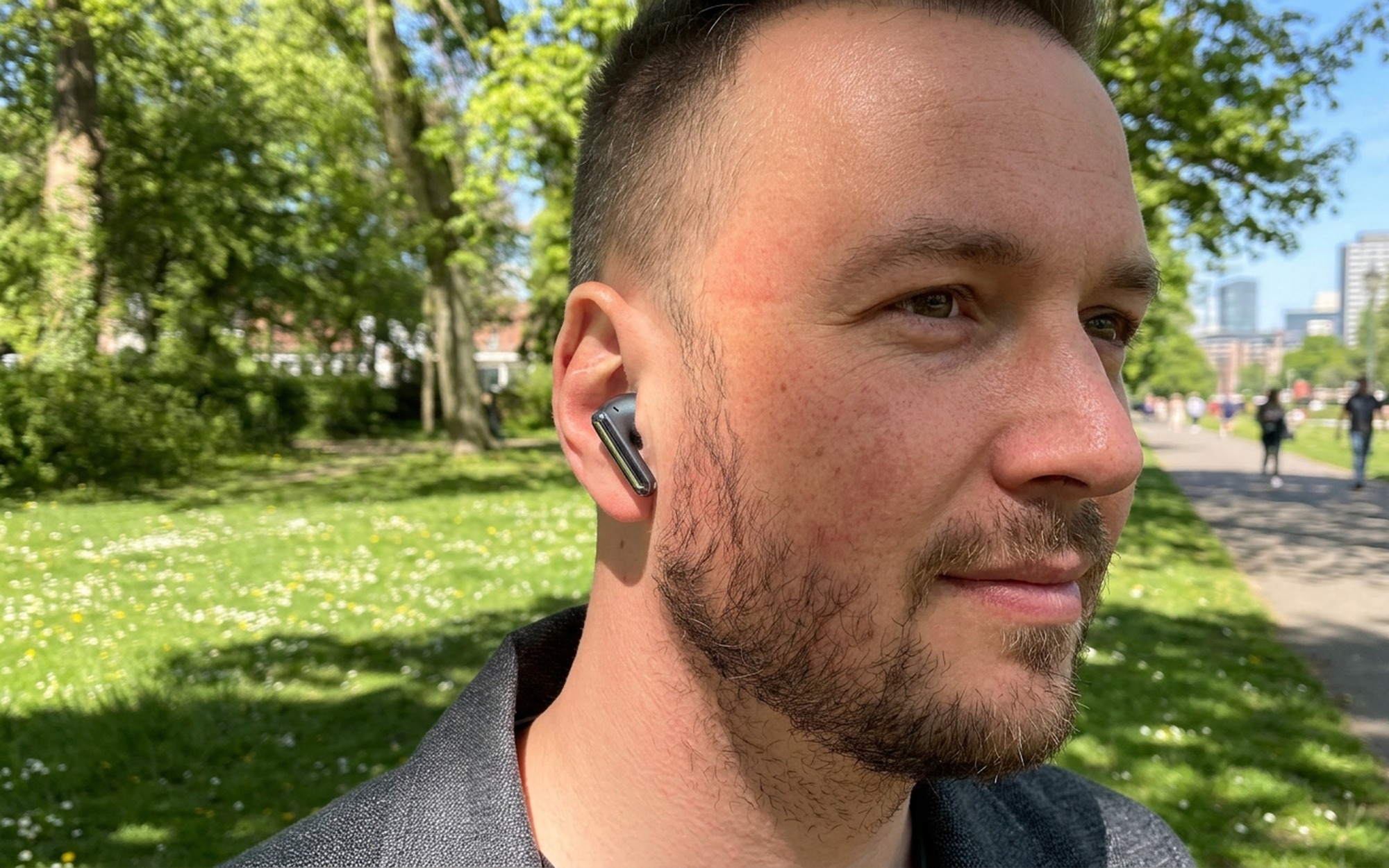 Person wearing Redmi Buds 8 Pro earbuds outdoors on sunny day with city background arm resting on bench