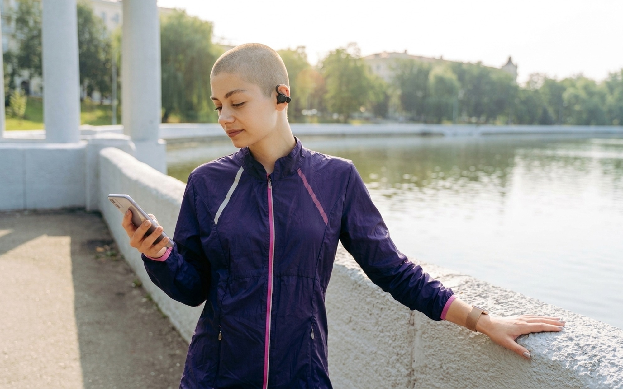 Young woman wearing Sony LinkBuds Clip earbuds outdoors in a city park on a sunny afternoon for lifestyle fitness review
