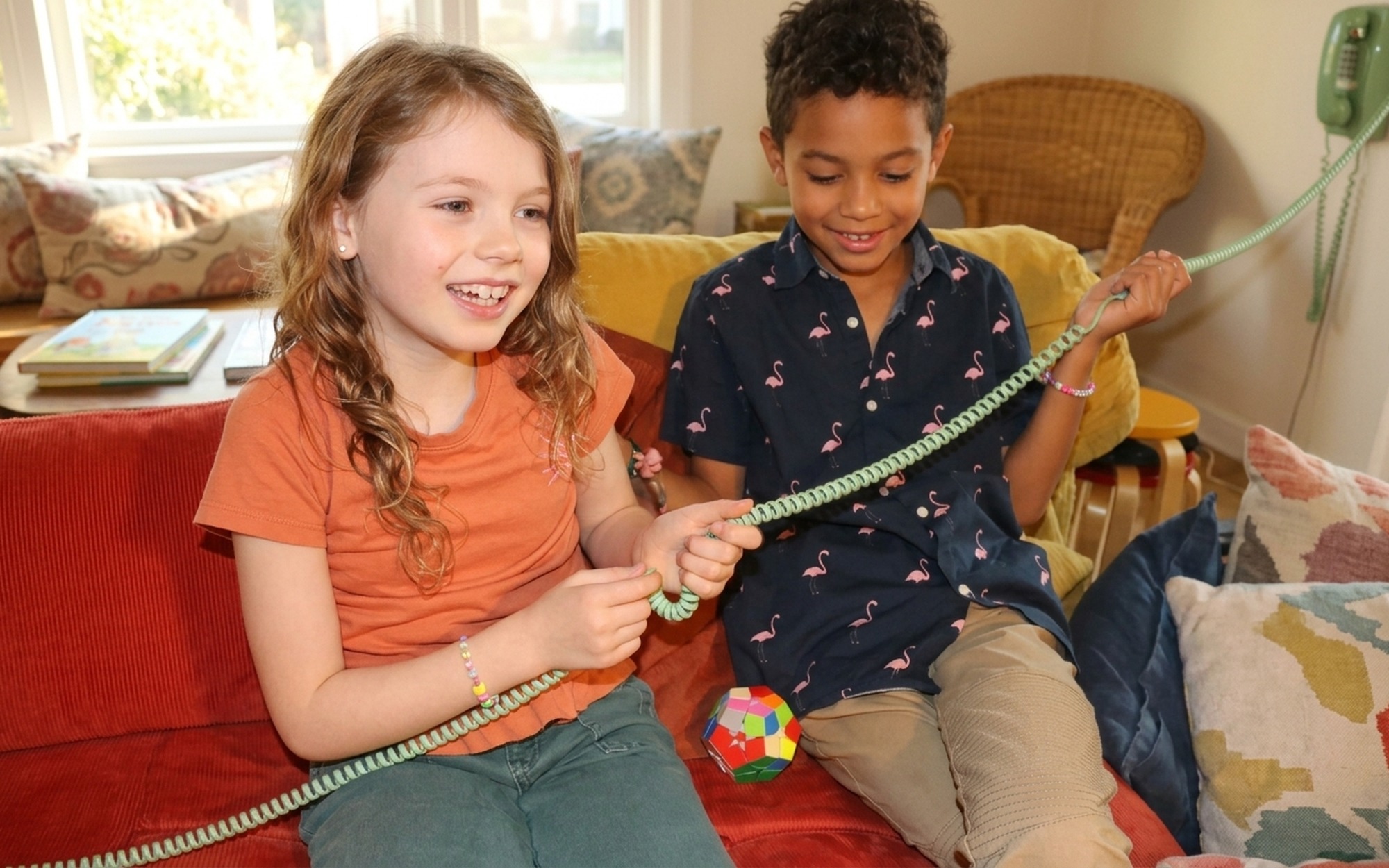 Two young children laughing together while using the Tin Can corded phone in a cozy home living room