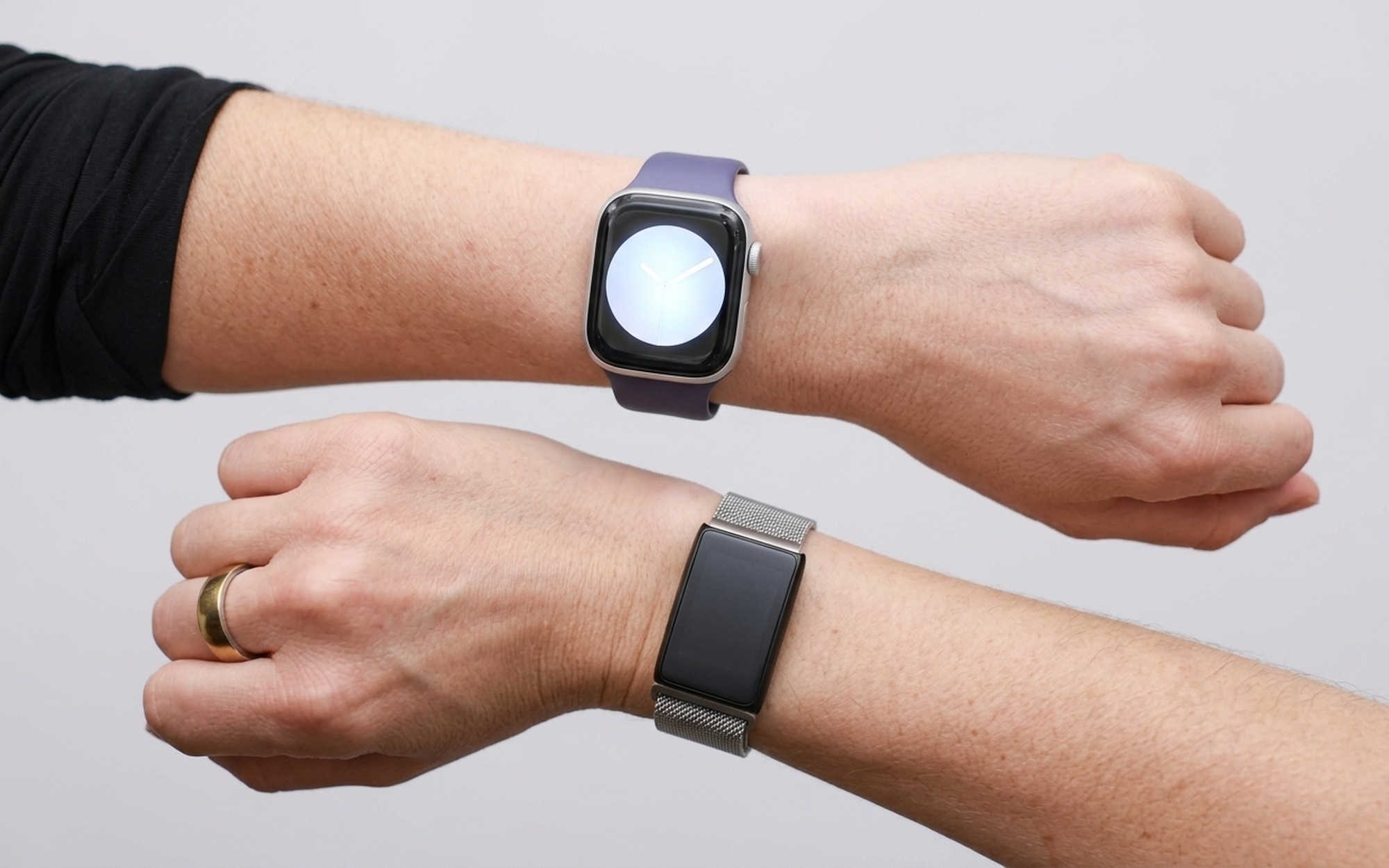 Side-by-side wrist comparison of a smartwatch with a large display versus a slim screenless WHOOP fitness band, both on separate wrists in natural daylight