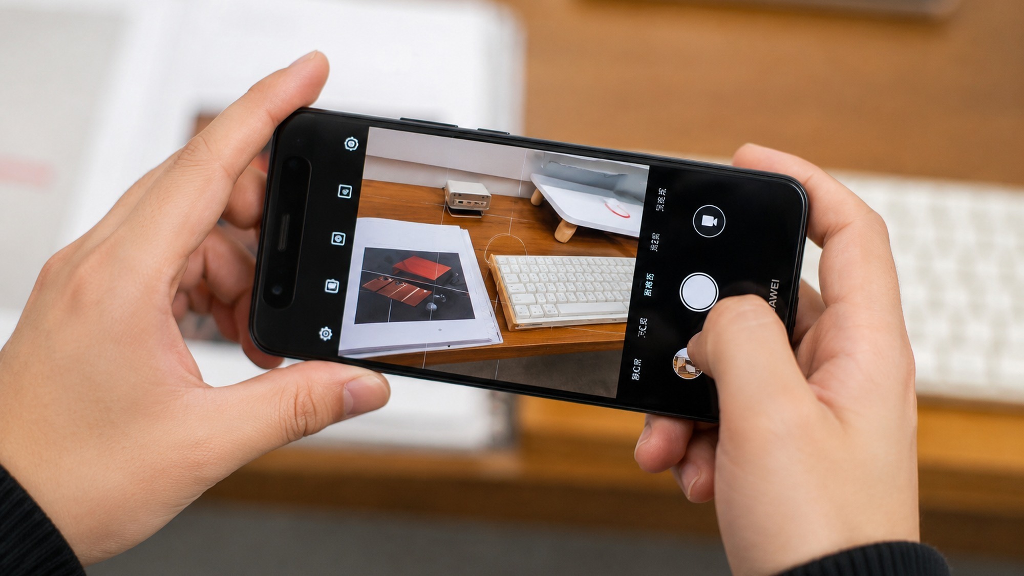 Two hands holding the Huawei nova 16 Ultra in landscape with the camera app open, framing a desk scene for a camera test.