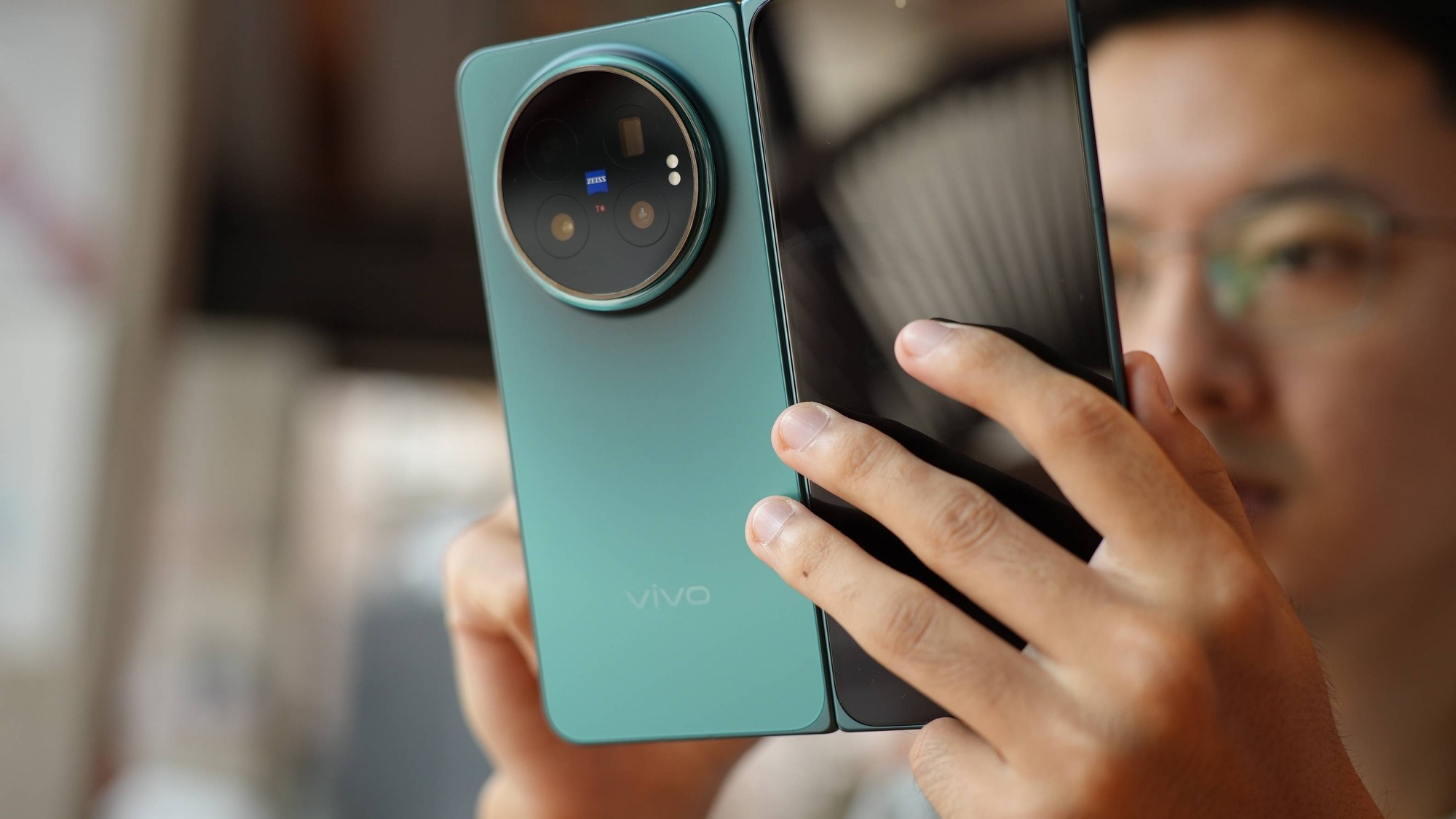 Close-up of the vivo X Fold6 ZEISS camera module on the teal model held half open in one hand